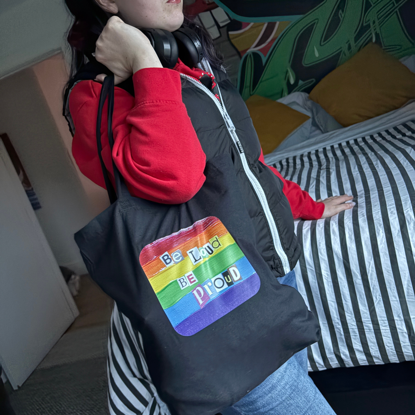 Black tote bag with rainbow pride design and text 'Be Loud Be Proud' held by a person.