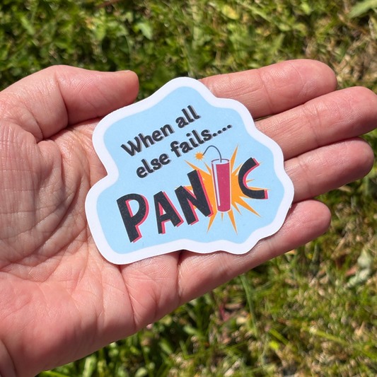 Hand holding a sticker with 'When all else fails... PANIC' text against a grassy background