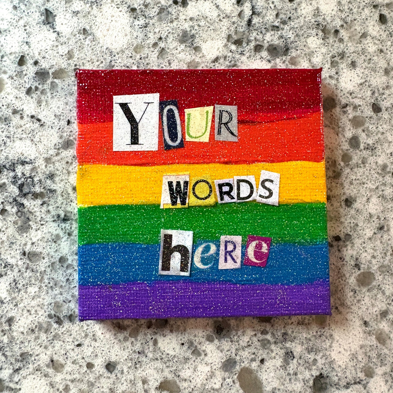 Colorful rainbow block with text reading "your words here" on a textured, glittery surface