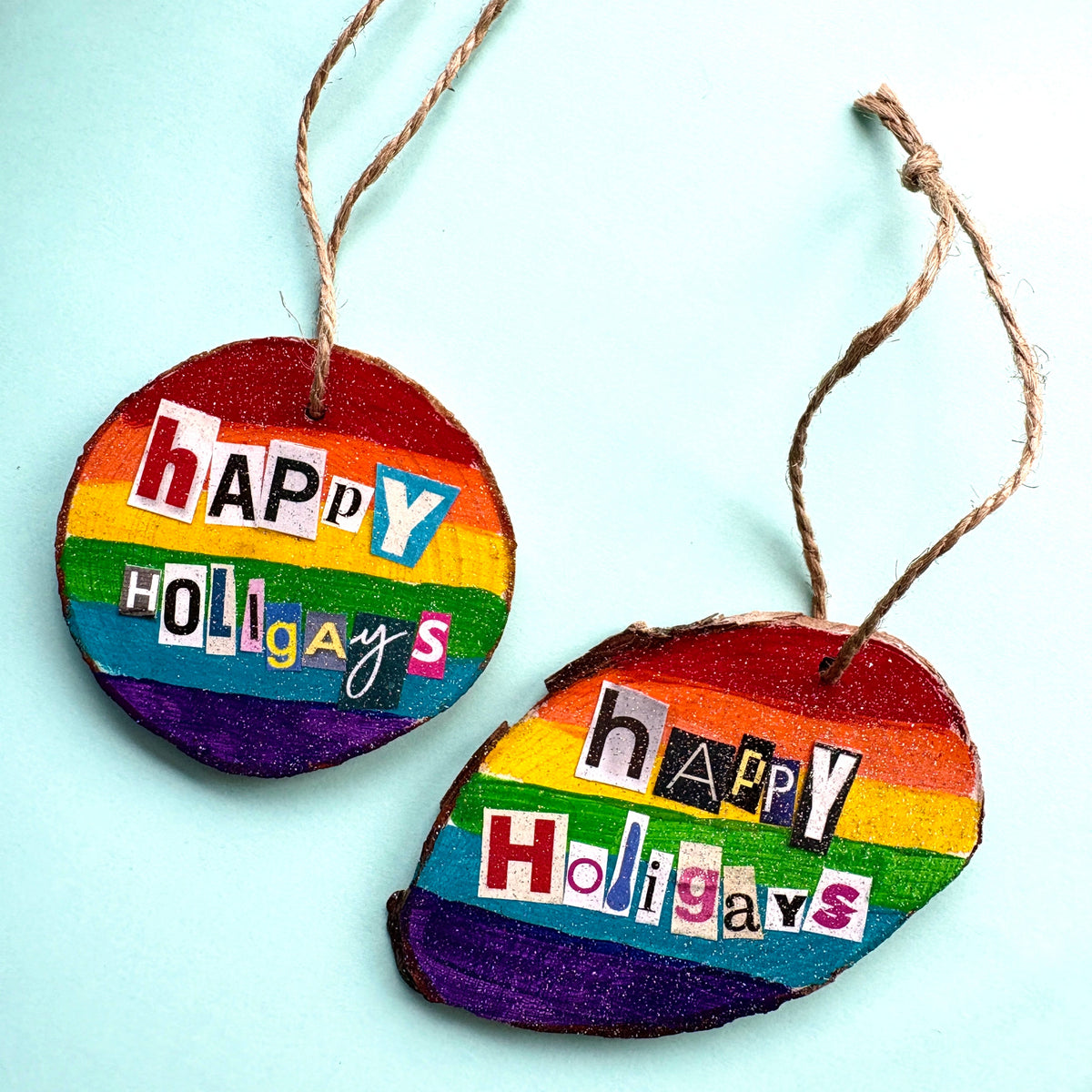 two wooden christmas decorations, hand painted with a rainbow background. Each has the words Happy Holigays spelled out in hand placed collage lettering.