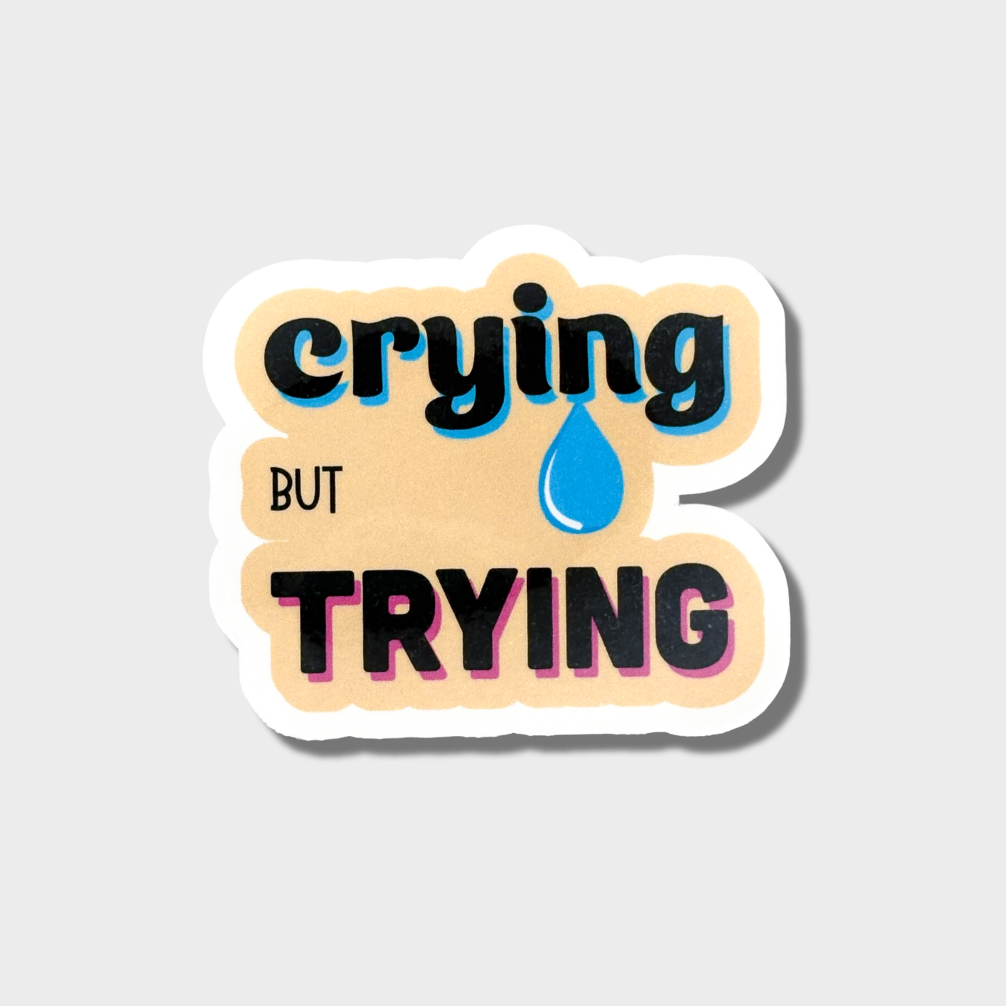 Sticker with 'crying but trying' text on a light gray background