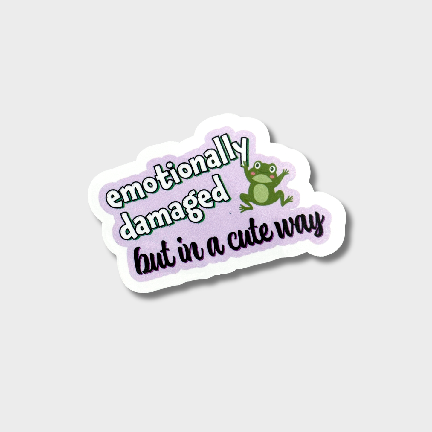 Sticker with text 'emotionally damaged but in a cute way' and a frog graphic on a light purple background