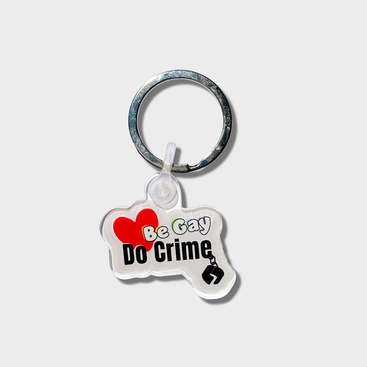 Keychain with 'Be Gay, Do Crime' text on a light grey background