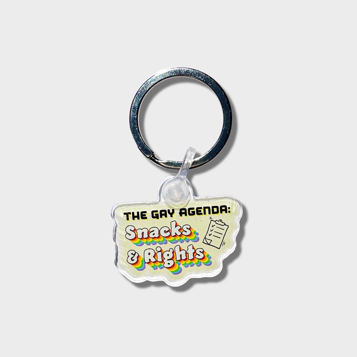 Keychain with 'The Gay Agenda: Snacks & Rights' text on a light yellow background
