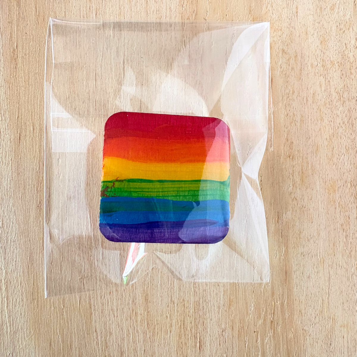 Rainbow-colored pin in a clear plastic bag on a wooden surface