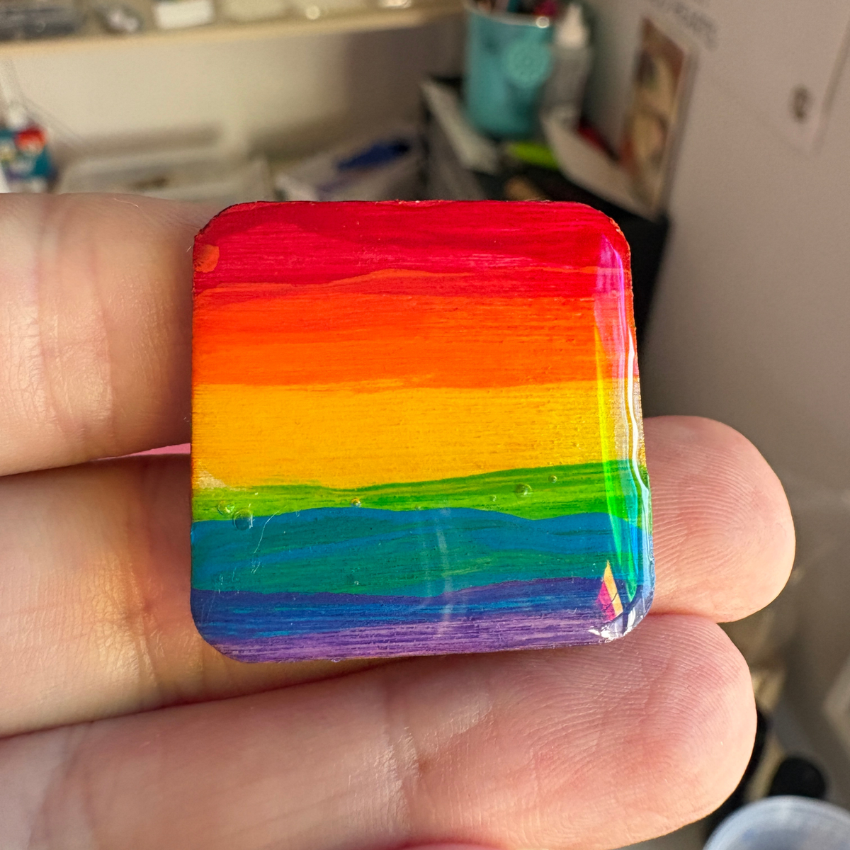 rainbow pride pin held in a hand with a blurred background