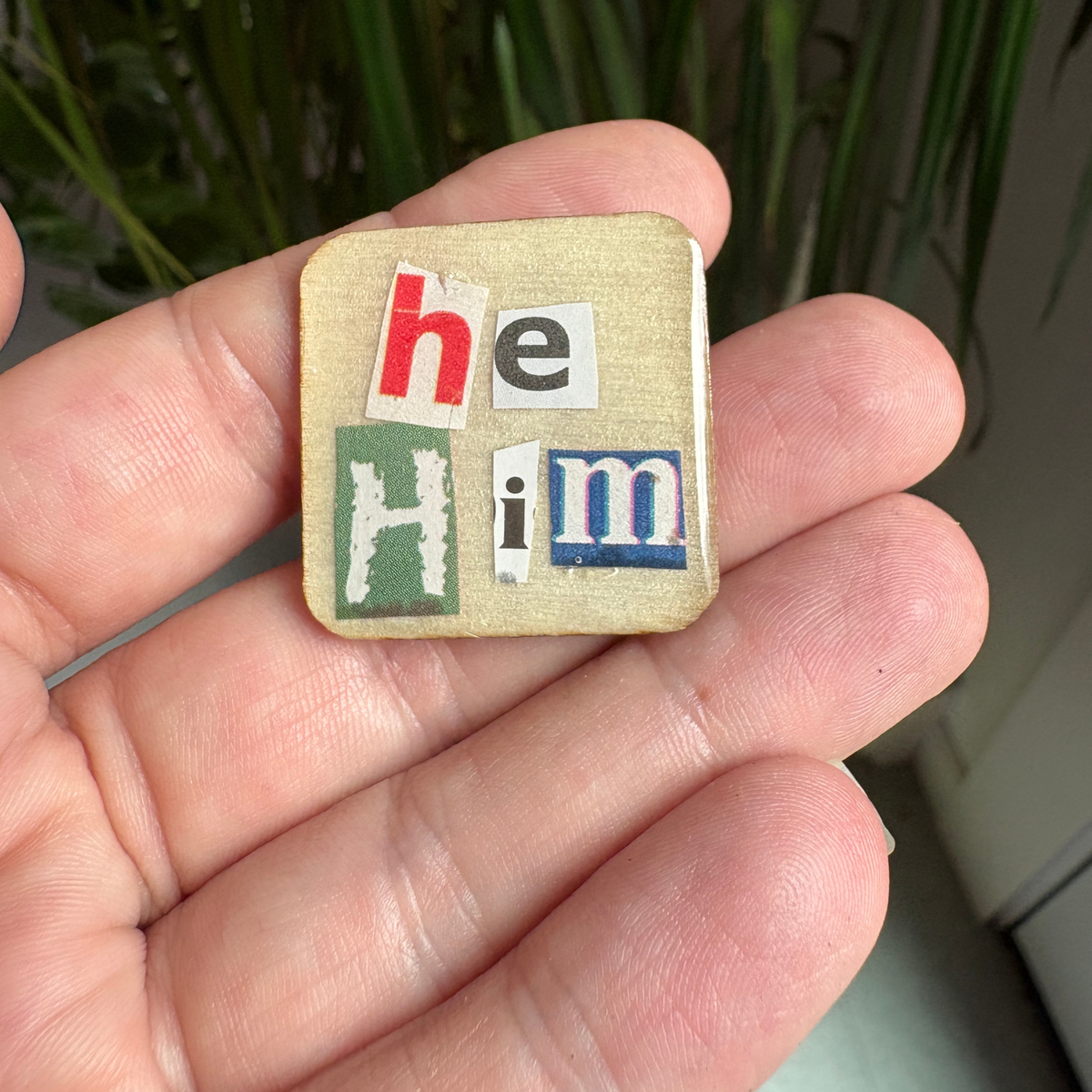 Patch with 'he him' text held in a hand against a blurred green background
