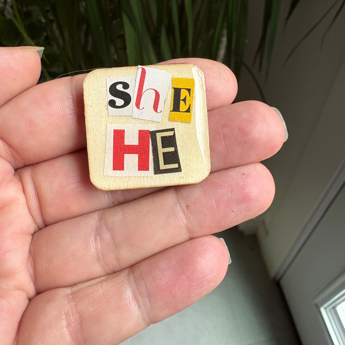 Small square object with 'SHE' and 'HE' text held in a hand.
