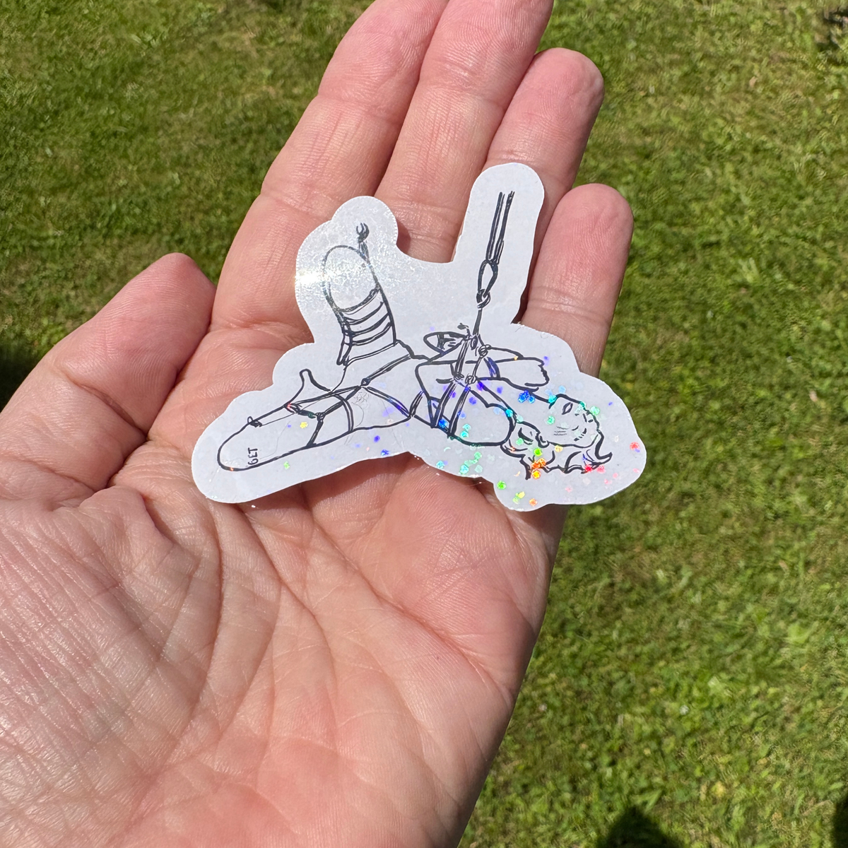 Hand holding a sticker with a person in a partial suspension on a grassy background