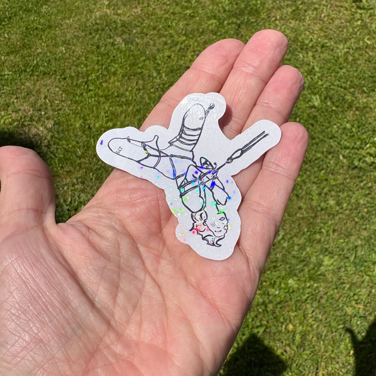 Hand holding a sticker of a person in a partial suspension against a grassy background