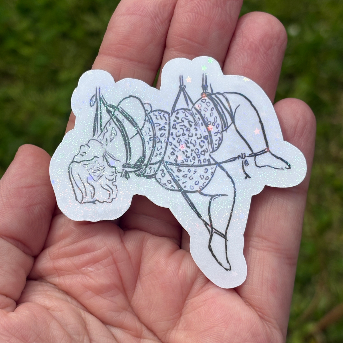 Hand holding a sticker with a design of a person in a rope suspension on a grassy background