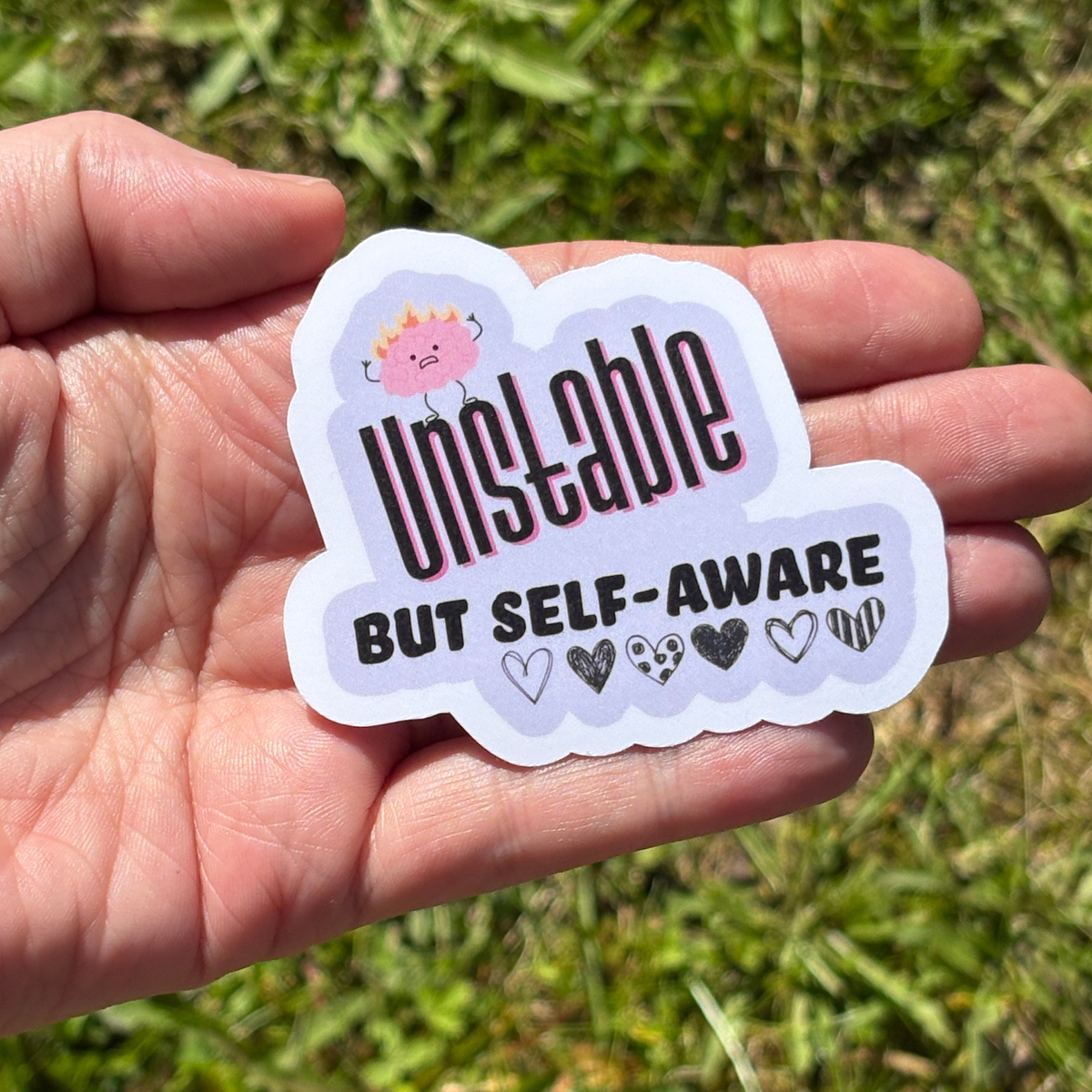 Sticker  that says "unstable but self aware" with a grassy background