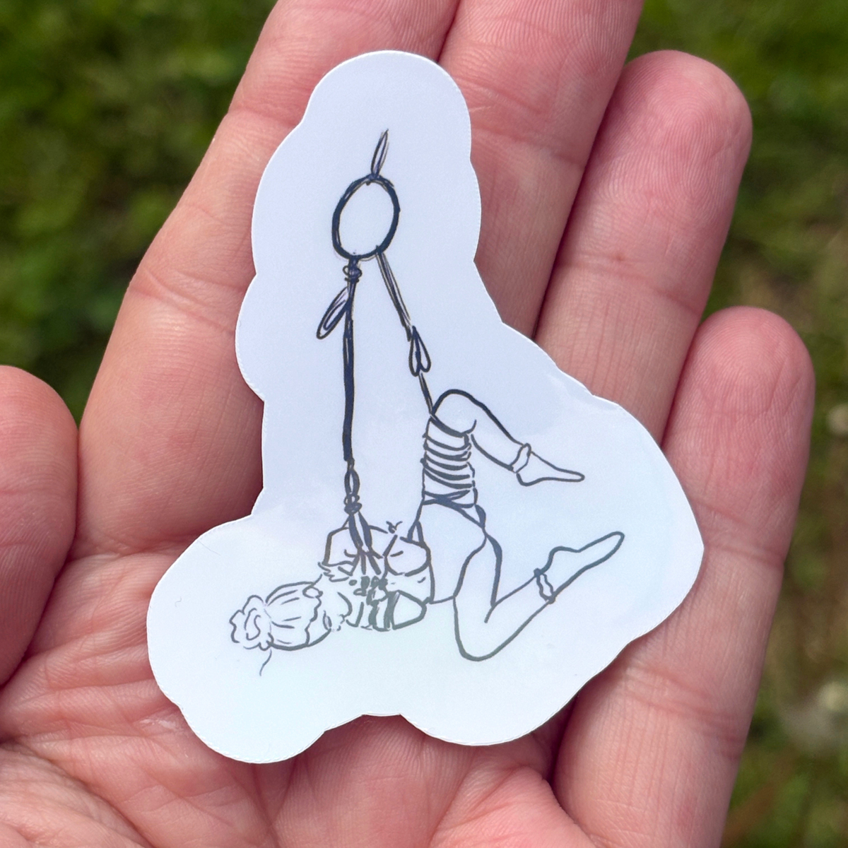 Hand holding a white sticker with a black line drawing of a person in a rope suspension.