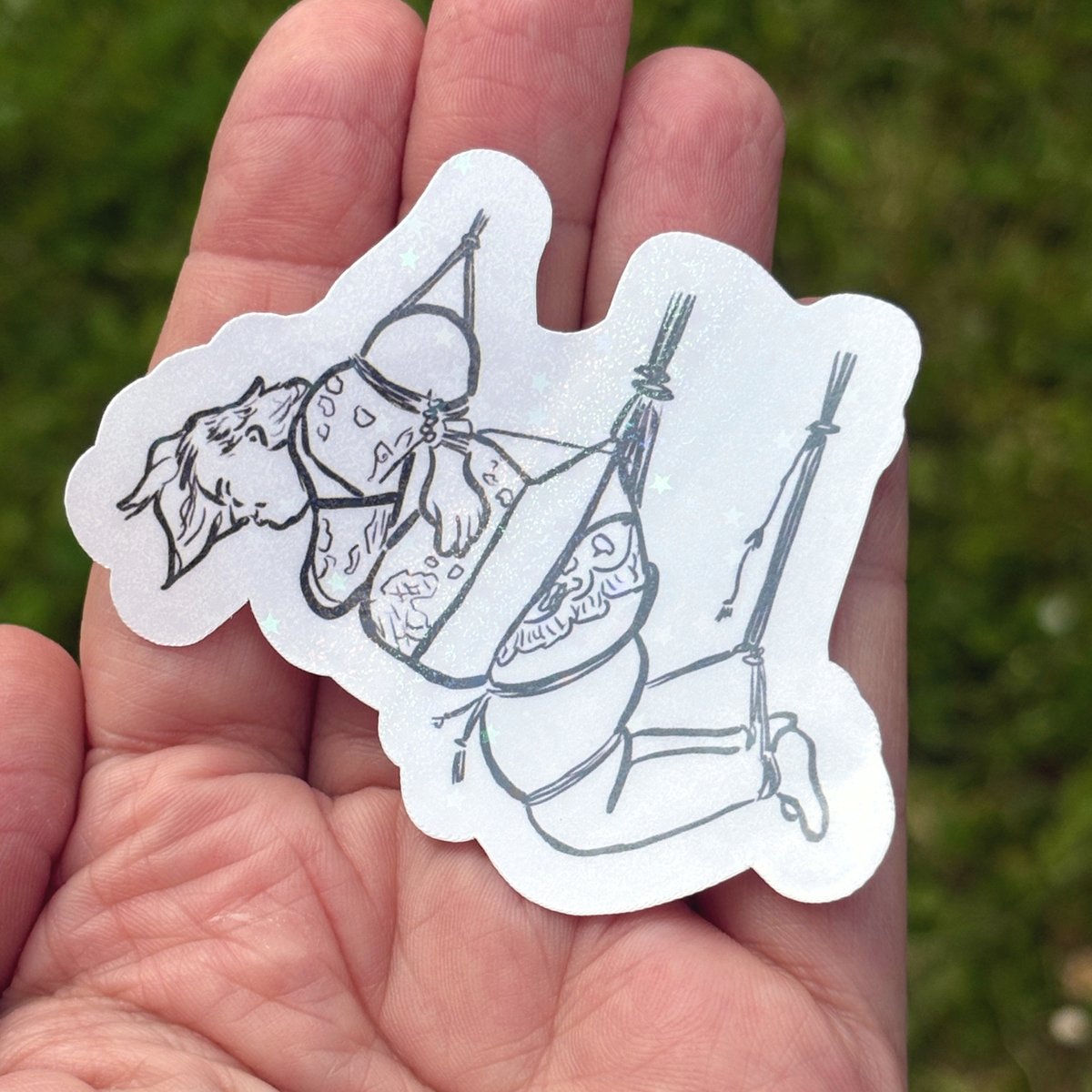 White sticker with black line art of a person in a face down rope suspension held in a hand against a grassy background