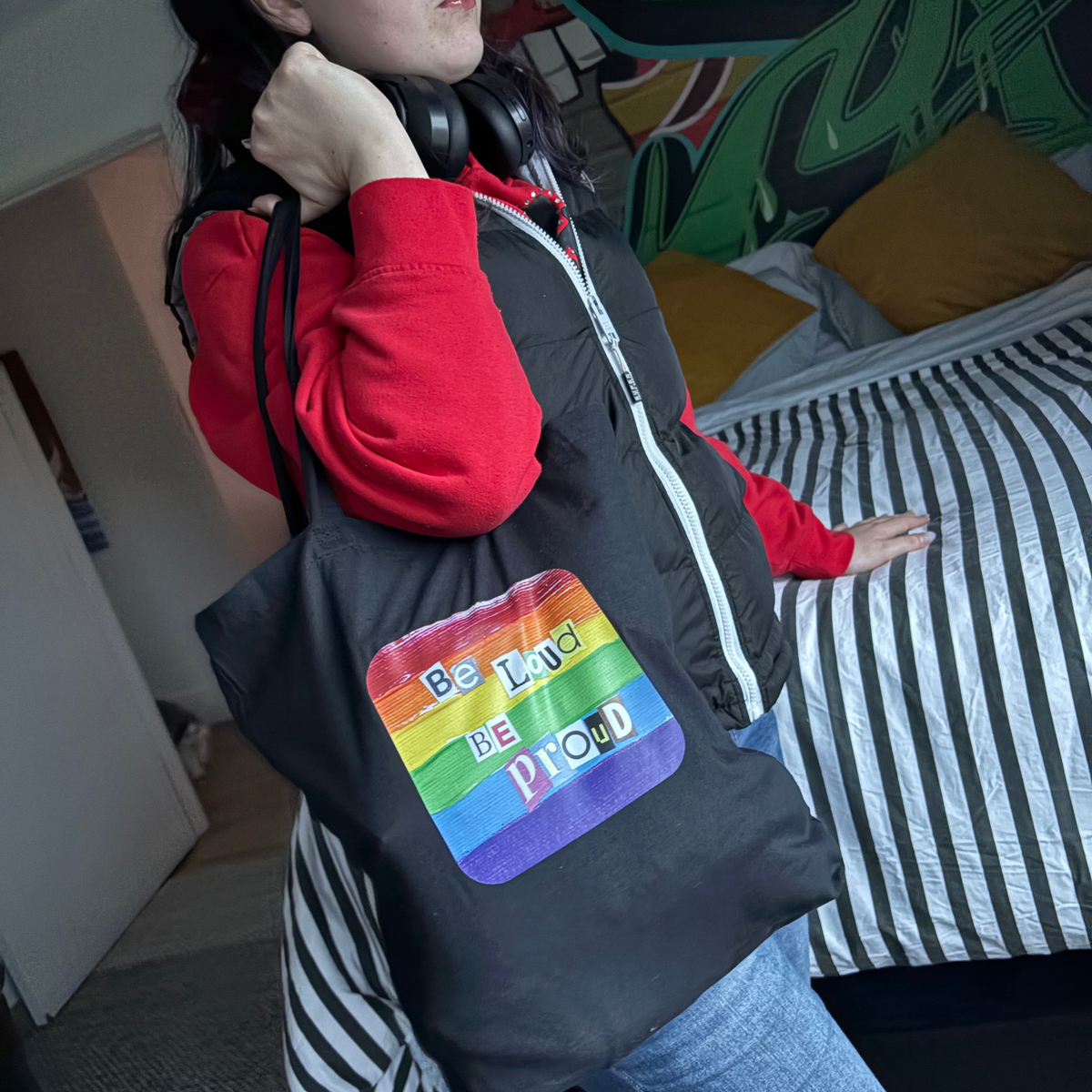 Black tote bag with rainbow pride design and text 'Be Loud Be Proud' held by a person.