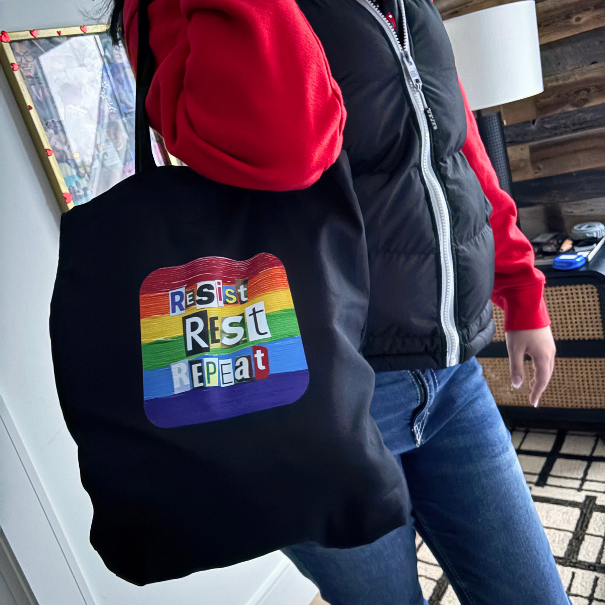 Person carrying a black tote with a rainbow-colored 'Resist Rest Repeat' design.